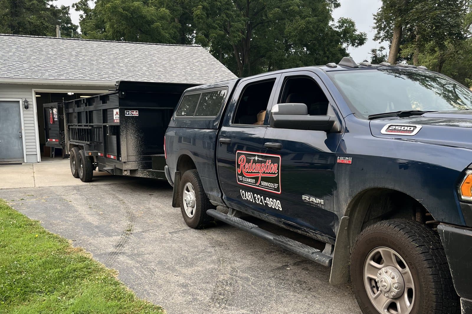 Redemption's branded truck and dump trailer backed up to an open garage on a residential driveway.