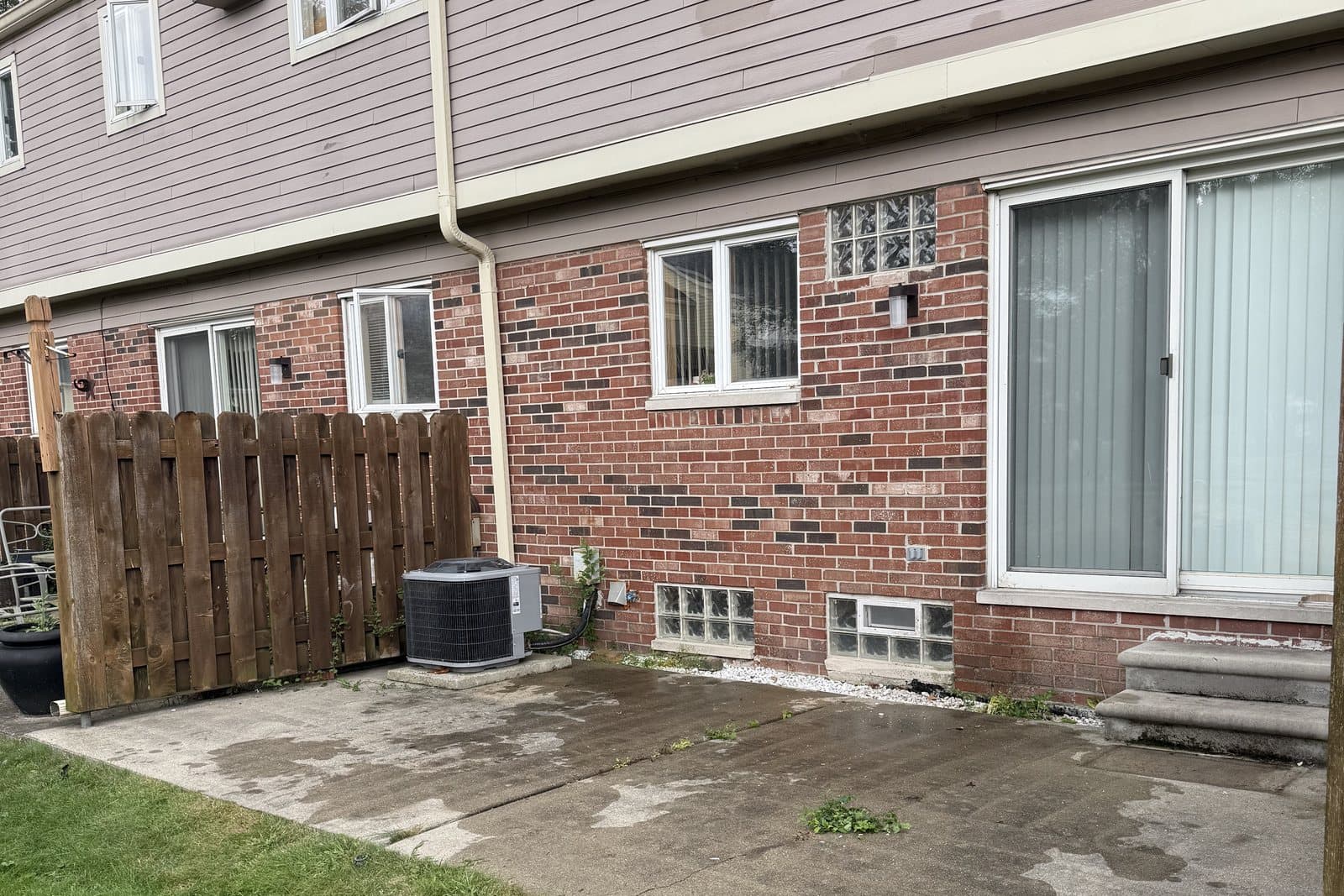 After: The same townhouse patio cleared and swept, with the brick wall, windows, and fence unchanged.