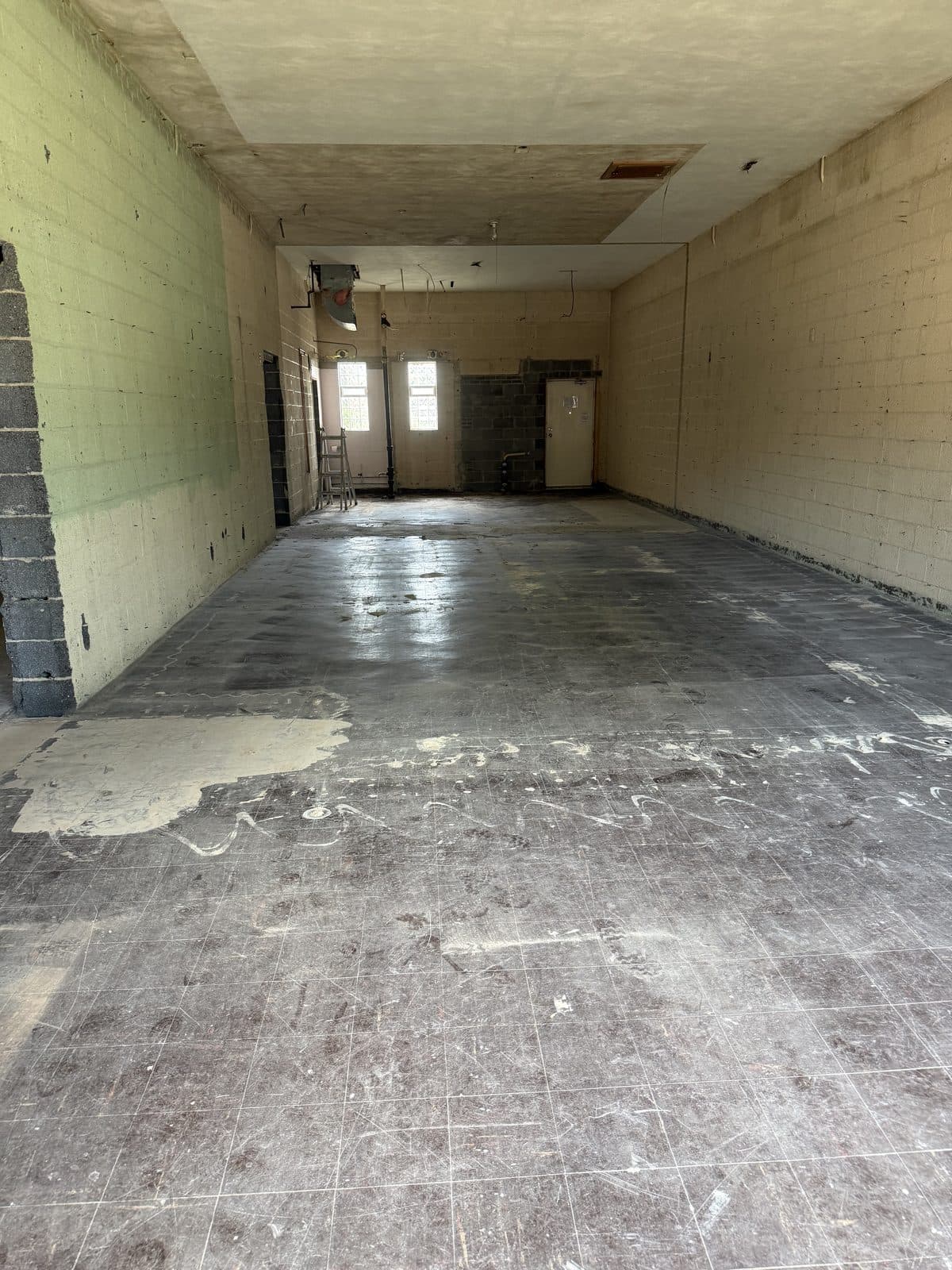 The stripped interior looking toward the rear windows, with the slab exposed and the ceiling open.
