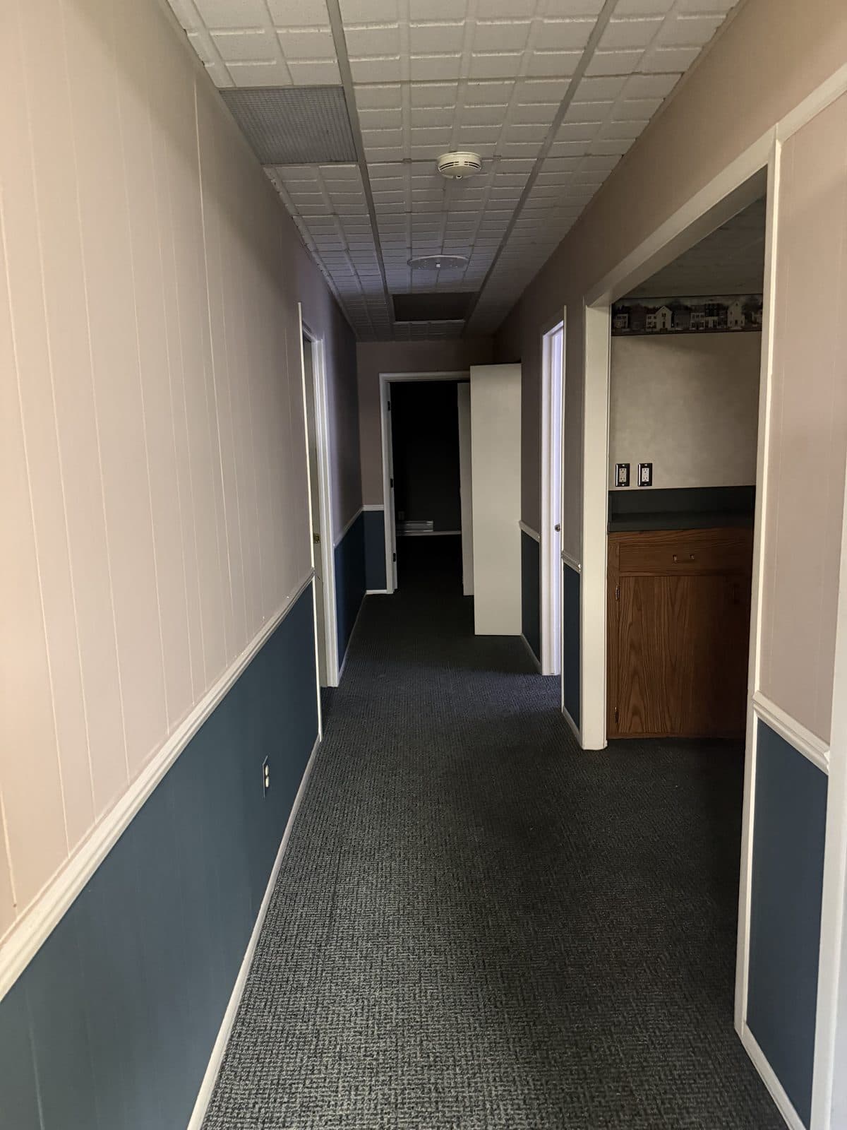 A carpeted office corridor lined with doorways and a built-in counter, before demolition.
